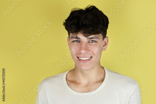 A handsome guy smiles gently on a yellow background, the teenager has a nice appearance and white healthy teeth because he had braces on his teeth. Portrait of a happy teenage boy