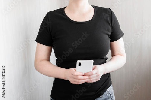 Girl wear black slim fit t-shirt standing and holding smartphone. Tee mock up with space for your design.