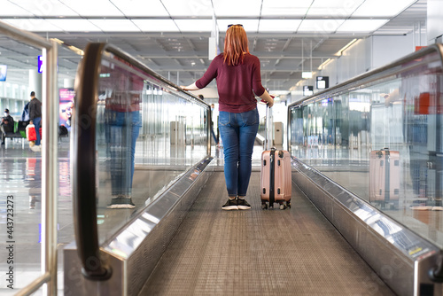 woman passenger with luggage in international airport or modern train station walking to gate.