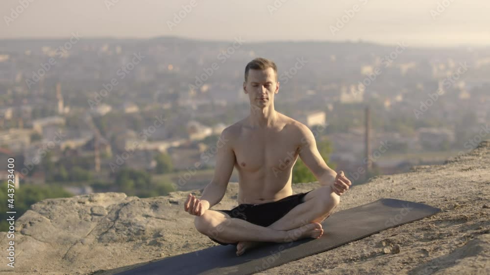 Peaceful shirtless man sitting on yoga mat and practicing lotus pose with closed eyes. Concept of people, sport activity and nature, mindfullness Peaceful shirtless man sitting on yoga mat and practicing lotus pose with closed eyes. Concept of people, sport activity and nature, mindfullness