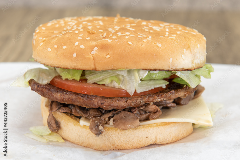 Mushroom swiss cheese burger loaded with lettuce and tomato inside a sesame seed bun.