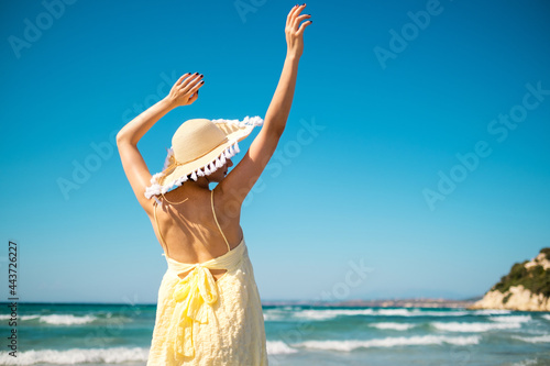 Woman with straw hat and yellow dress on the beach and arms streched. photo