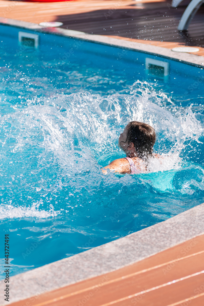 the child has fun jumping into the water from the side of the pool and sending splashes of water around, enjoying a vacation and a hot summer. 