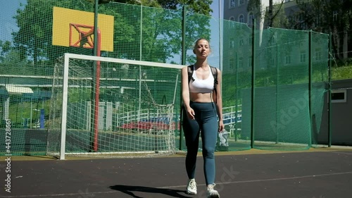 young fit athletic blond busty woman with ponytail in sportswear walking at sports ground. attractive caucasian female walks through football playground. fitness training outdoors, healthy lifestyle photo