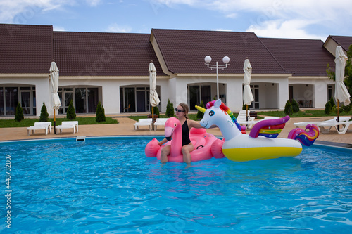Happy woman relaxing joyful sunbathing at infinity swimming pool with flamingo float and unicorn. Tourist sunbathing in swimsuit on luxury hotel.