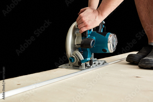 Sawing plywood by circular saw. Home repair. Hand tool. Man hold equipment. Building process. Woodworking. Safety engineering. Without gloves. Copy space. Indoor. Cutting material. Rental instrument