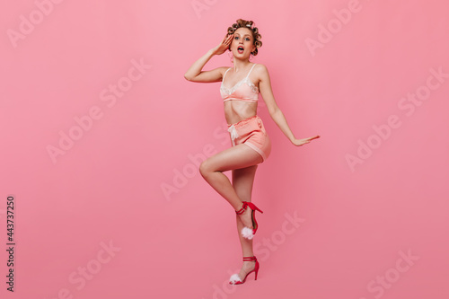 Blonde girl in pin-up pajamas salutes against pink background