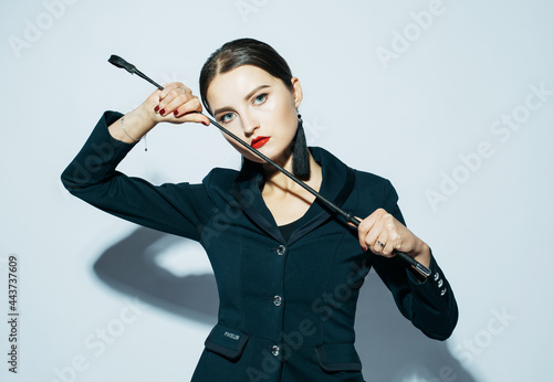 Young beautiful dominant lady posing in black outfit and holding a whip photo