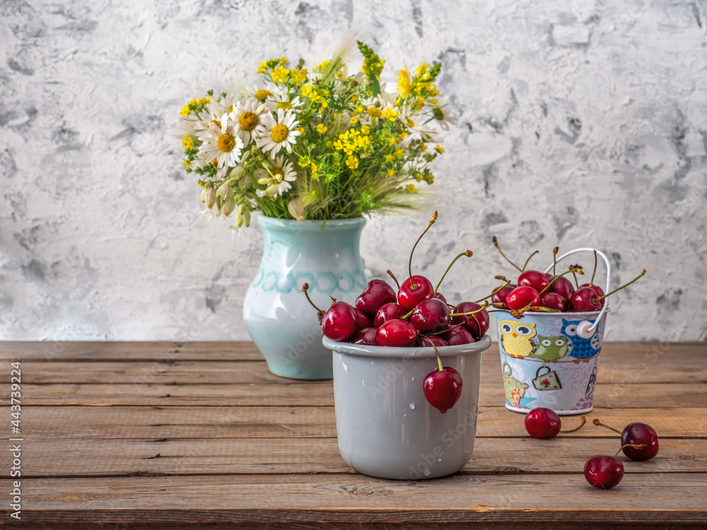 Summer still life with cherries and wildflowers in a field vase on a wooden table