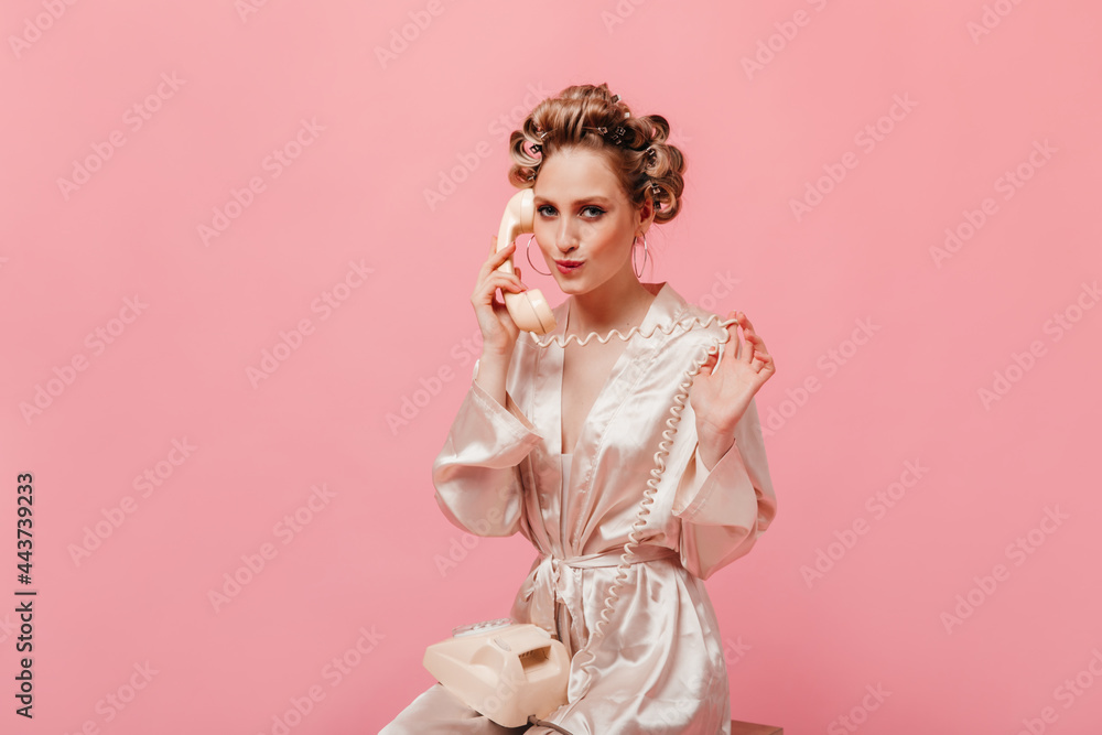 Beautiful woman in silk dressing gown coquettishly talking on phone on pink background Beautiful woman in silk dressing gown coquettishly talking on phone on pink background