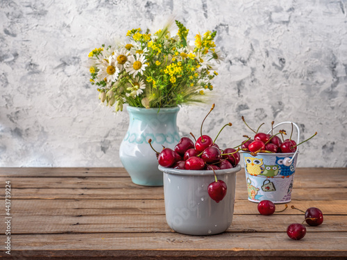 Summer still life with cherries and wildflowers in a field vase on a wooden table