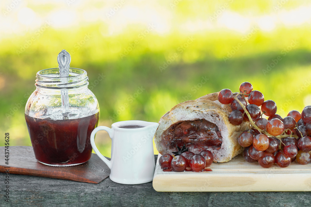 Bread stuffed with grapes jam with some grapes fruits, syrup and jar of jam over wood boards. With copy space and green blurred background Bread stuffed with grapes jam with some grapes fruits, syrup and jar of jam over wood boards. With copy space and green blurred background