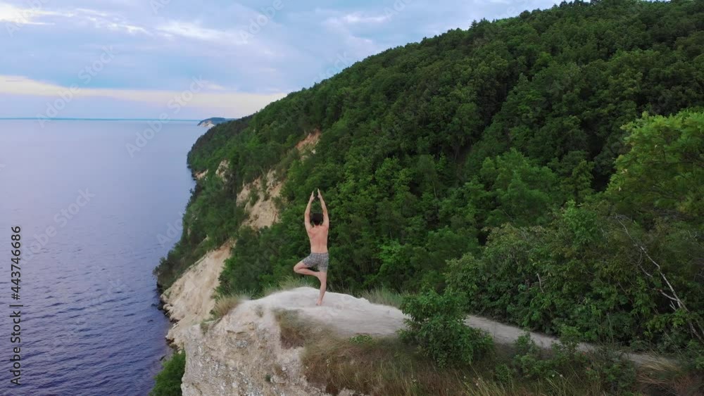 Young shirtless man meditating on a cliff around the forest in early morning Young shirtless man meditating on a cliff around the forest in early morning
