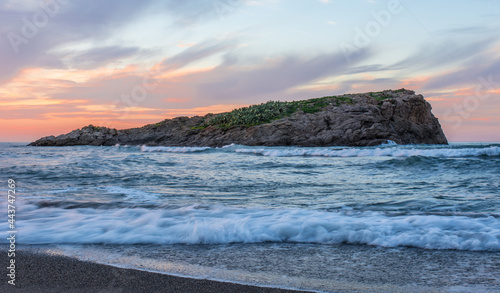 A small island in the middle of a rough sea, high waves, clouds, beautiful blue sky with sunset, Mediterranean sea, sandy beach.