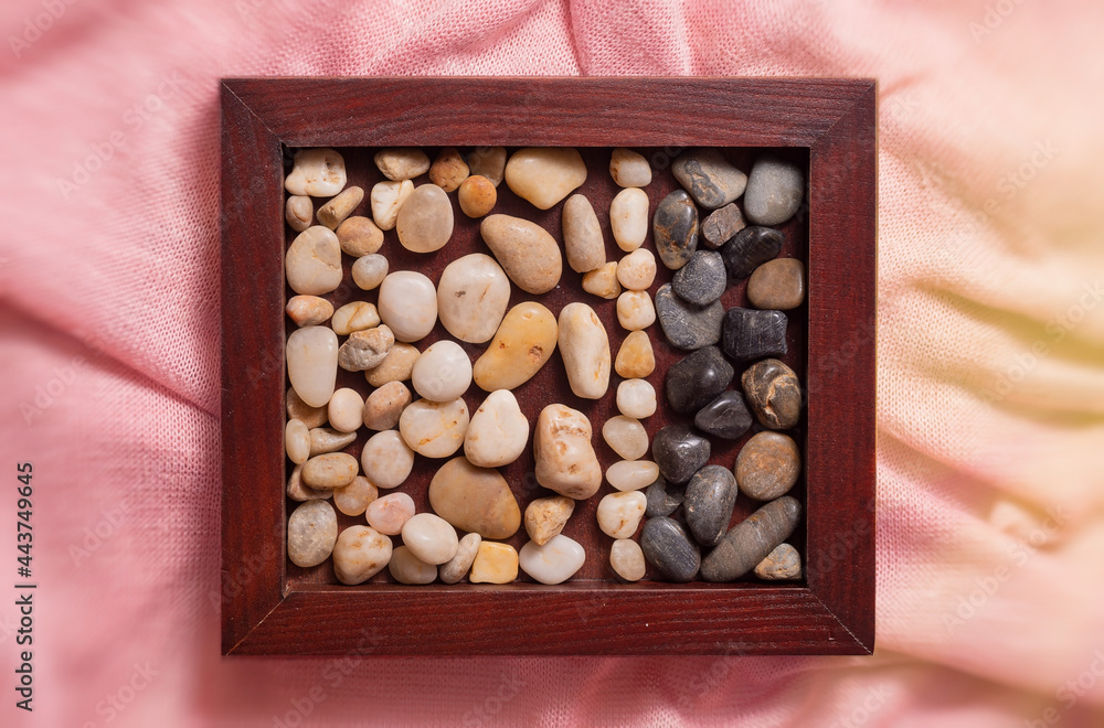 A wooden frame with sea pebbles on a pink fabric. A wooden frame with sea pebbles on a pink fabric.