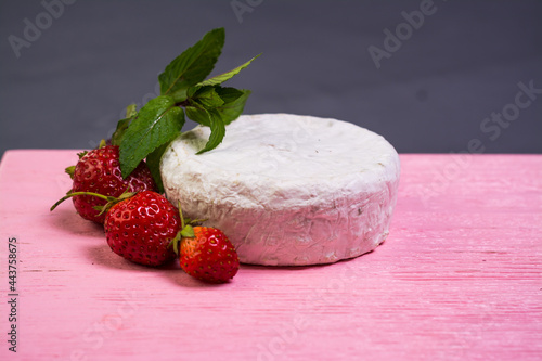Camembert with strawberries with mint on a pink wooden board on a grey background 