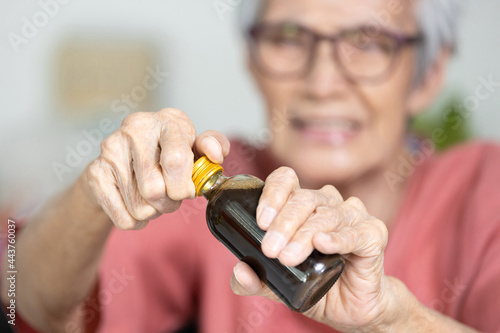 Asian senior woman hold a bottle of liquid drug,old elderly try to open the screw cap of bottle with difficulty,unscrew cap to open,hard to open,problem with weak hands or fingers,muscle weakness photo