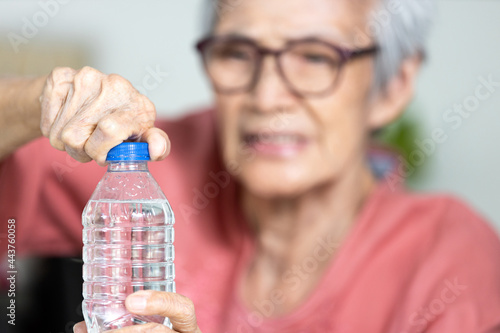 Trouble opening the bottle of drinking water in the elderly age,life problem,senior woman with numbness and weakness of hands and fingers muscle,difficulty in turning or unscrewing cap of water bottle photo