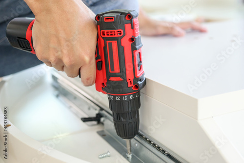 man assembling white table furniture at home using cordless screwdriver