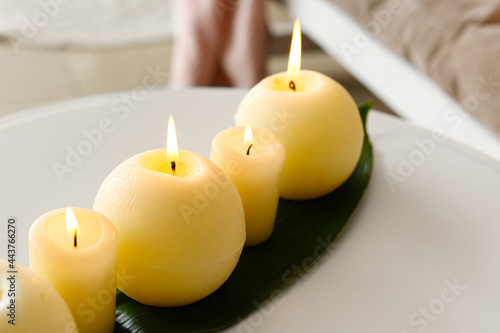 Burning candles with palm leaf on table in room, closeup