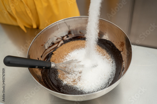 a person pours a good amount of white sugar into a bowl with chocolate and brown sugar. Concept of cooking, pastry.