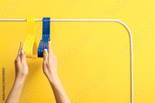 Female hands with clothes hangers on rack against color background