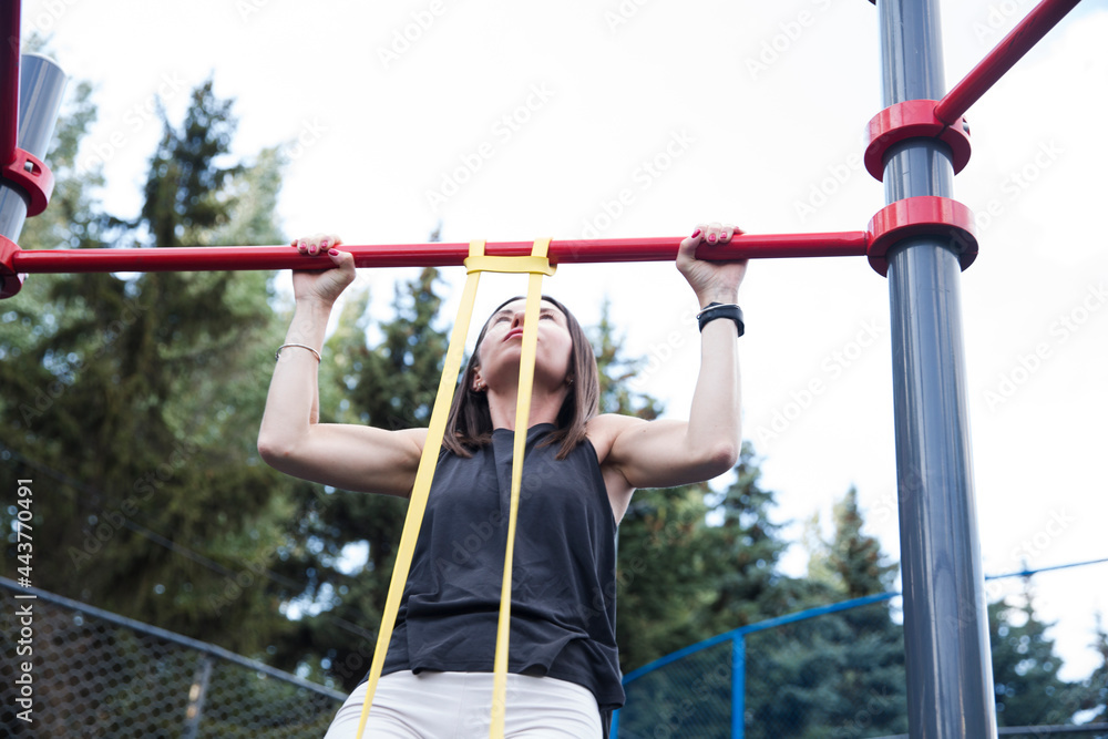 young woman in sport clothes doing pull ups on horizontal bar sport ground outdoors. training and lifestyle concept. street workout young woman in sport clothes doing pull ups on horizontal bar sport ground outdoors. training and lifestyle concept. street workout