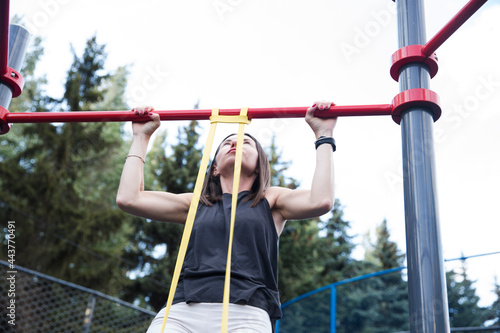 young woman in sport clothes doing pull ups on horizontal bar sport ground outdoors. training and lifestyle concept. street workout