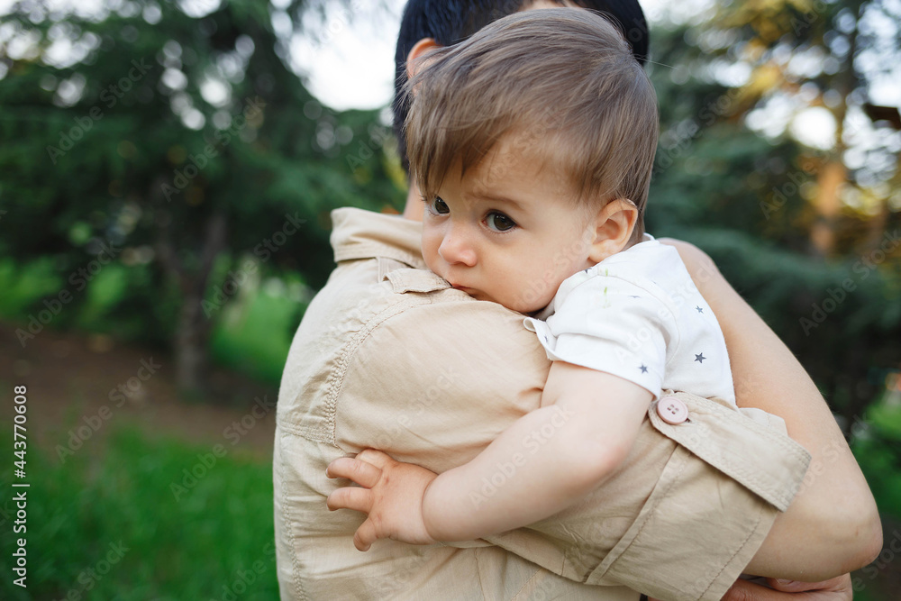 young mom hugs her little son while sitting in the park on the lawn young mom hugs her little son while sitting in the park on the lawn