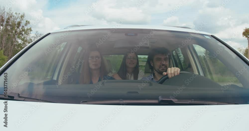Enjoying travel. Beautiful young couple sitting on the front passenger seats and smiling to each other while handsome man driving a car and their daughter sitting at the back seats Enjoying travel. Beautiful young couple sitting on the front passenger seats and smiling to each other while handsome man driving a car and their daughter sitting at the back seats