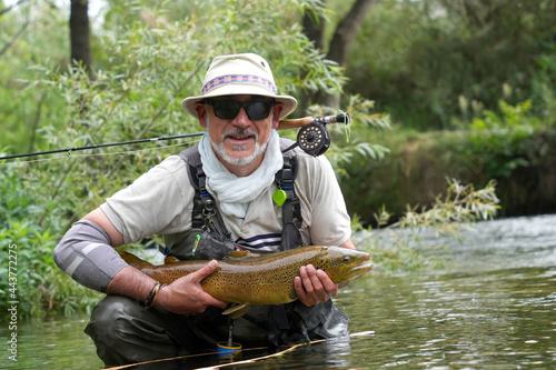 fly fisherman catching a big wild trout in a small river