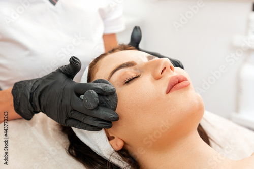 Cosmetology and beauty procedures. Professional beautician gives a facial massage with jade stones to the client in salon. Close up of female face. Concept of rejuvenation