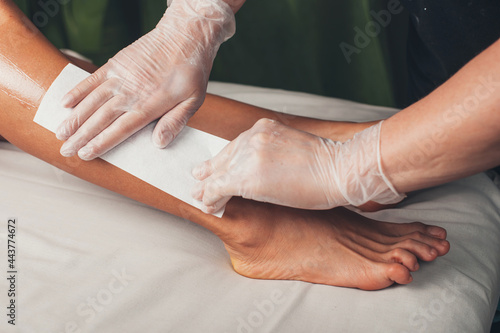 Close up photo of a caucasian spa worker having leg epilation procedures with a lying on the couch client photo