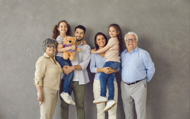 Studio photo shoot group portrait of cheerful big extended multi generational family against grey background.Happy smiling mom, dad, grandma, grandpa and two little kids all together looking at camera