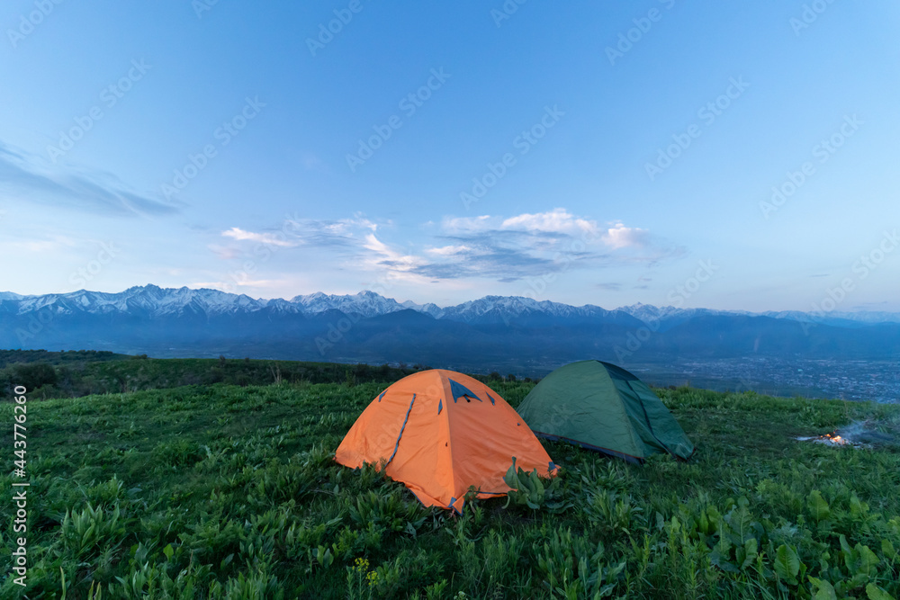 Two tents stand at the top of a green hill