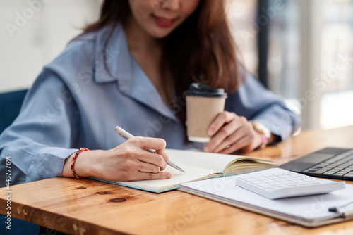 Close-up of a businesswoman holding a pen and taking notes at the office.