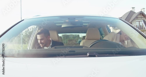 Front view of the caucasian husband and his wife sitting into the car and fastened with safety belts while preparing to the traveling. People and transport concept