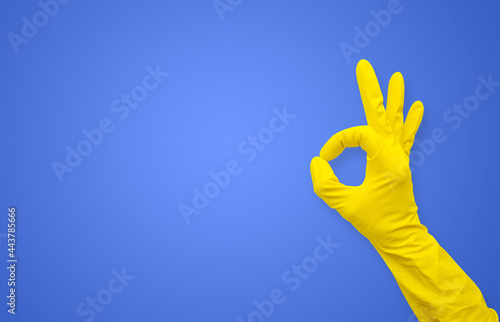 Hand in a yellow rubber glove shows the gesture "okay" on a blue background with copy space
