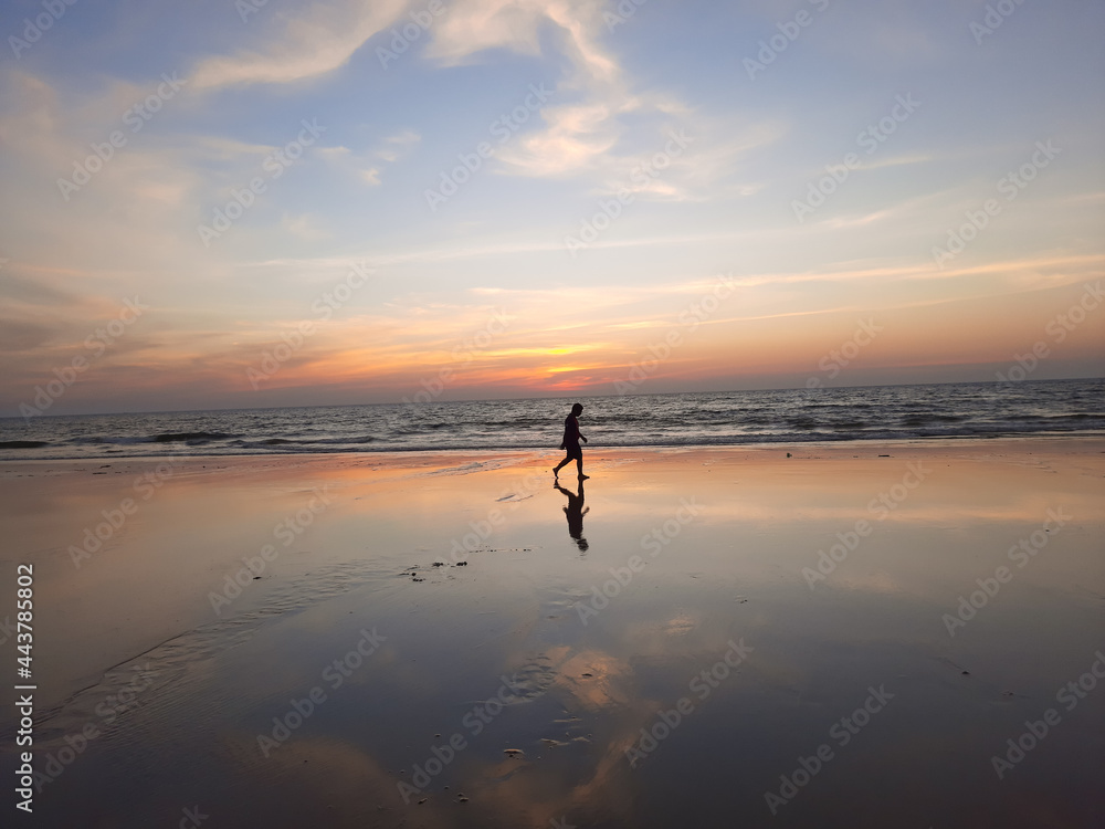 silhouette of a person on the beach, A calm and tranquil zen-like sunset at the beach with beautiful colours in blue and red with reflections on the water.