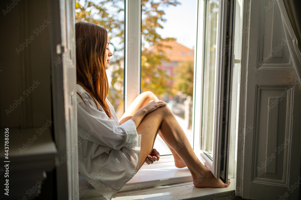 Pensive dreamy girl sitting in window relaxing in modern cozy loft bedroom alone Pensive dreamy girl sitting in window relaxing in modern cozy loft bedroom alone