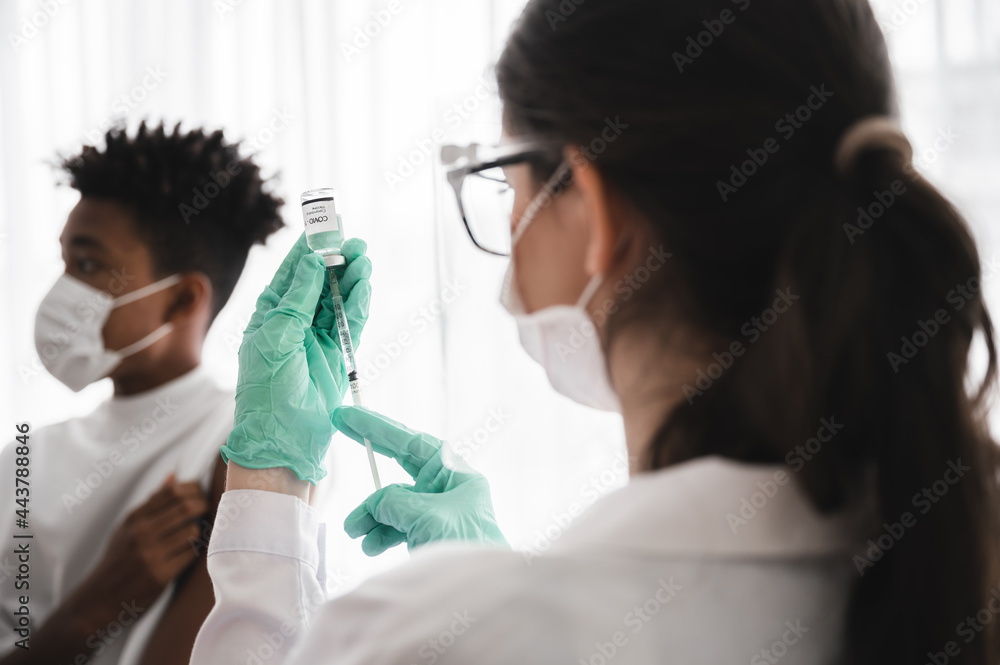 Female doctor or nurse wearing mask, gloves, and visor preparing to vaccinate coronavirus 19 to immunize African-American men.Concepts to prevent the spread of COVID-19. Female doctor or nurse wearing mask, gloves, and visor preparing to vaccinate coronavirus 19 to immunize African-American men.Concepts to prevent the spread of COVID-19.