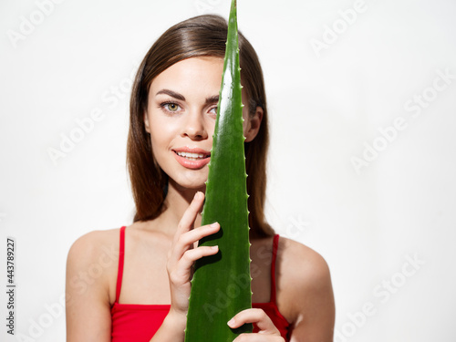 portrait of a woman with aloe leaf in front of her face on a light background clear skin
