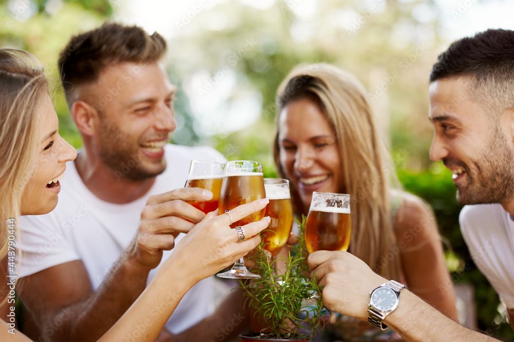 Group of happy friends toasting with beer at the summer bar. Selective focus on on the glass