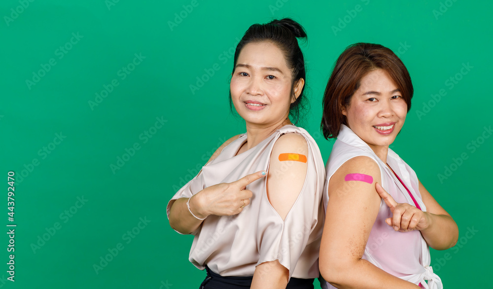 Two middle aged Asian women showing their arms with bandage patch showing they got vaccinated for Covid 19 virus on green background. Concept for Covid 19 vaccination Two middle aged Asian women showing their arms with bandage patch showing they got vaccinated for Covid 19 virus on green background. Concept for Covid 19 vaccination