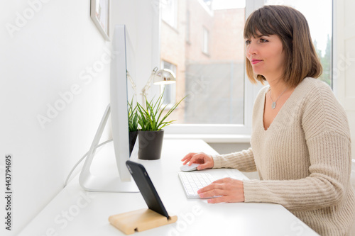 Beautiful professional businesswoman working with desktop computer in office. Photo of young woman sit indoors at home working on computer. © AndyPhoton