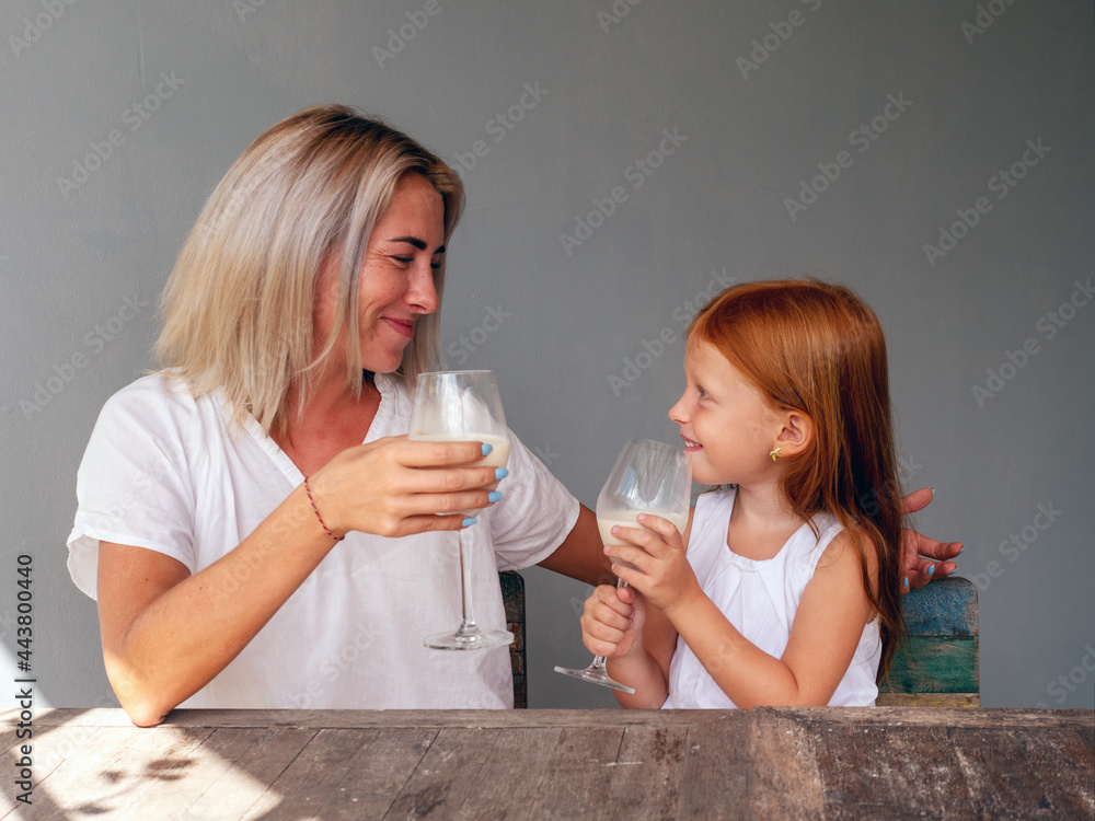 Mom and six-year-old red-haired daughter drink milk at the table from glasses Mom and six-year-old red-haired daughter drink milk at the table from glasses