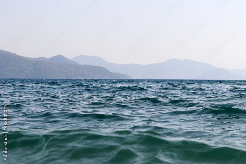 Scenic view from sea water surface to misty mountains covered with forest. Beach vacation, background for summer travel