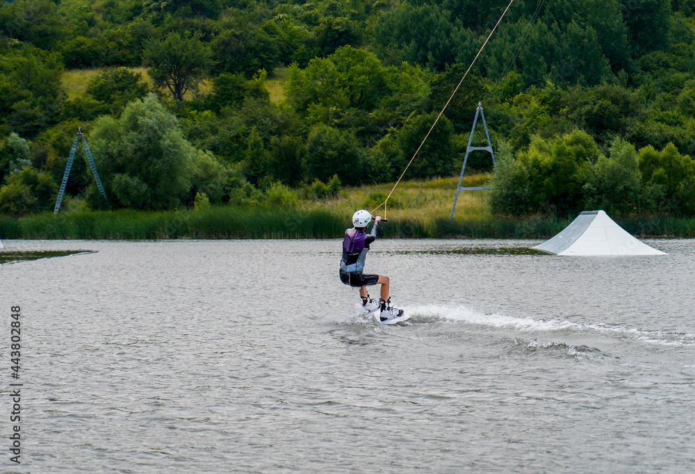 Woman practicing wakeboarding on a lake with green hills in cloudy day Woman practicing wakeboarding on a lake with green hills in cloudy day
