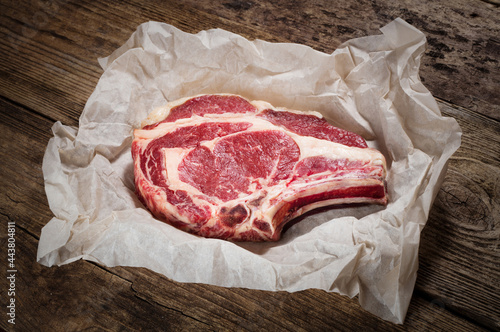 matured raw rib-eye steak in paper on wooden background