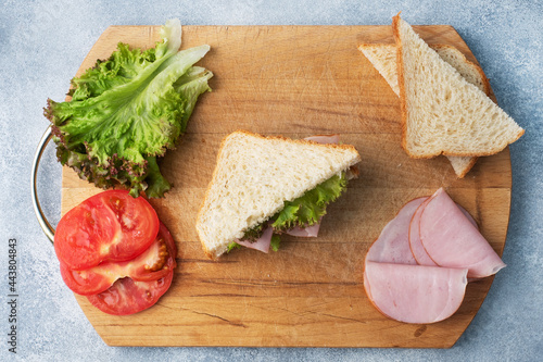 Delicious healthy sandwich for a snack breakfast on a wooden cutting board, top view. Toast bread tomato ham leaf salad.
